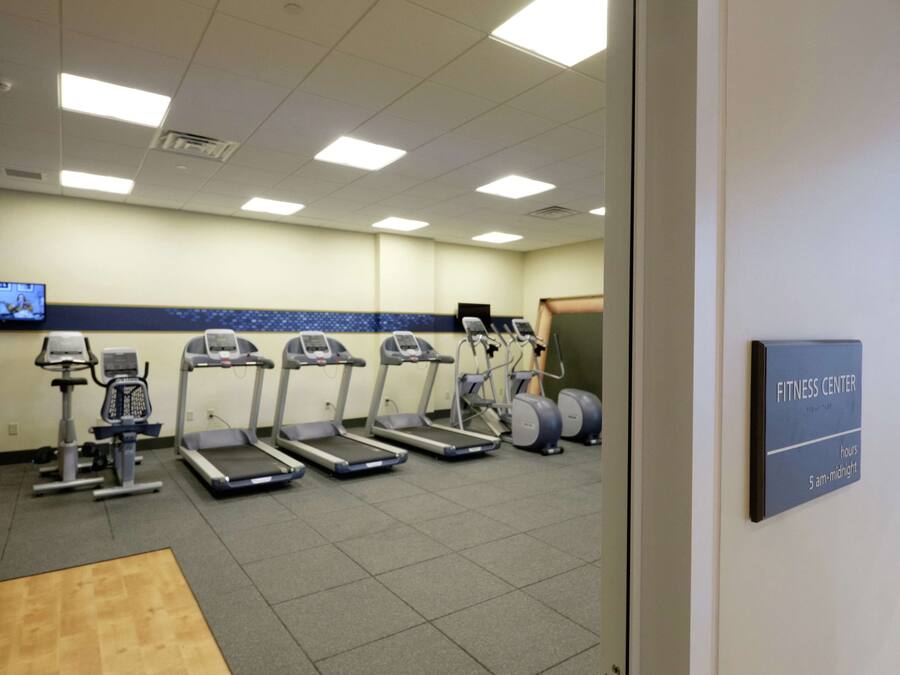 Een fitnessruimte met loopbanden, elliptische trainers en een televisiescherm.