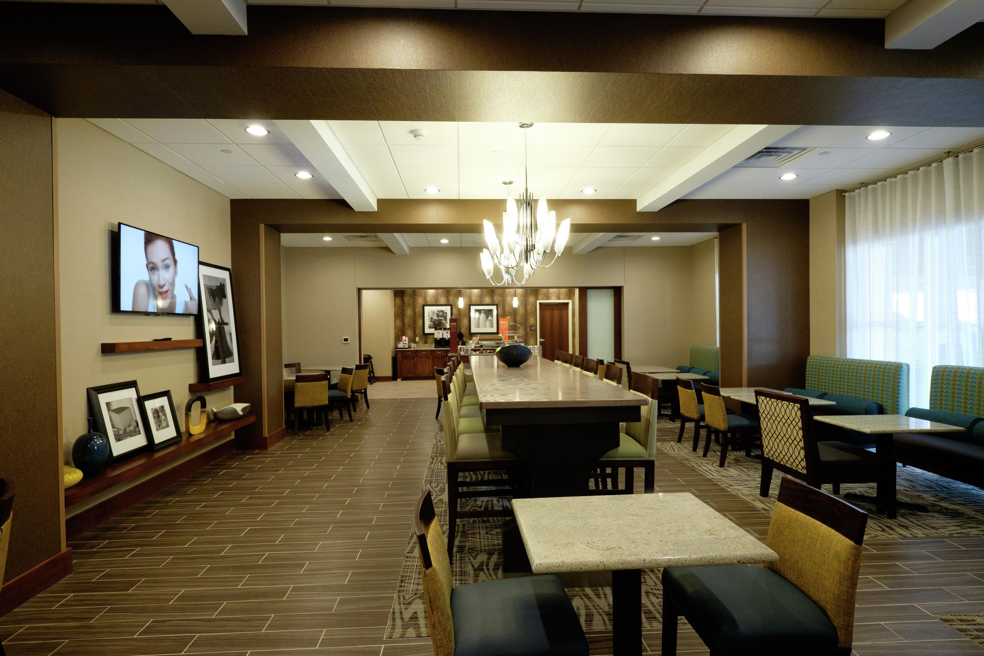 A hotel dining area with a long communal table, individual tables, and chairs.