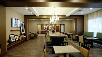 A hotel dining area with a long communal table, individual tables, and chairs.