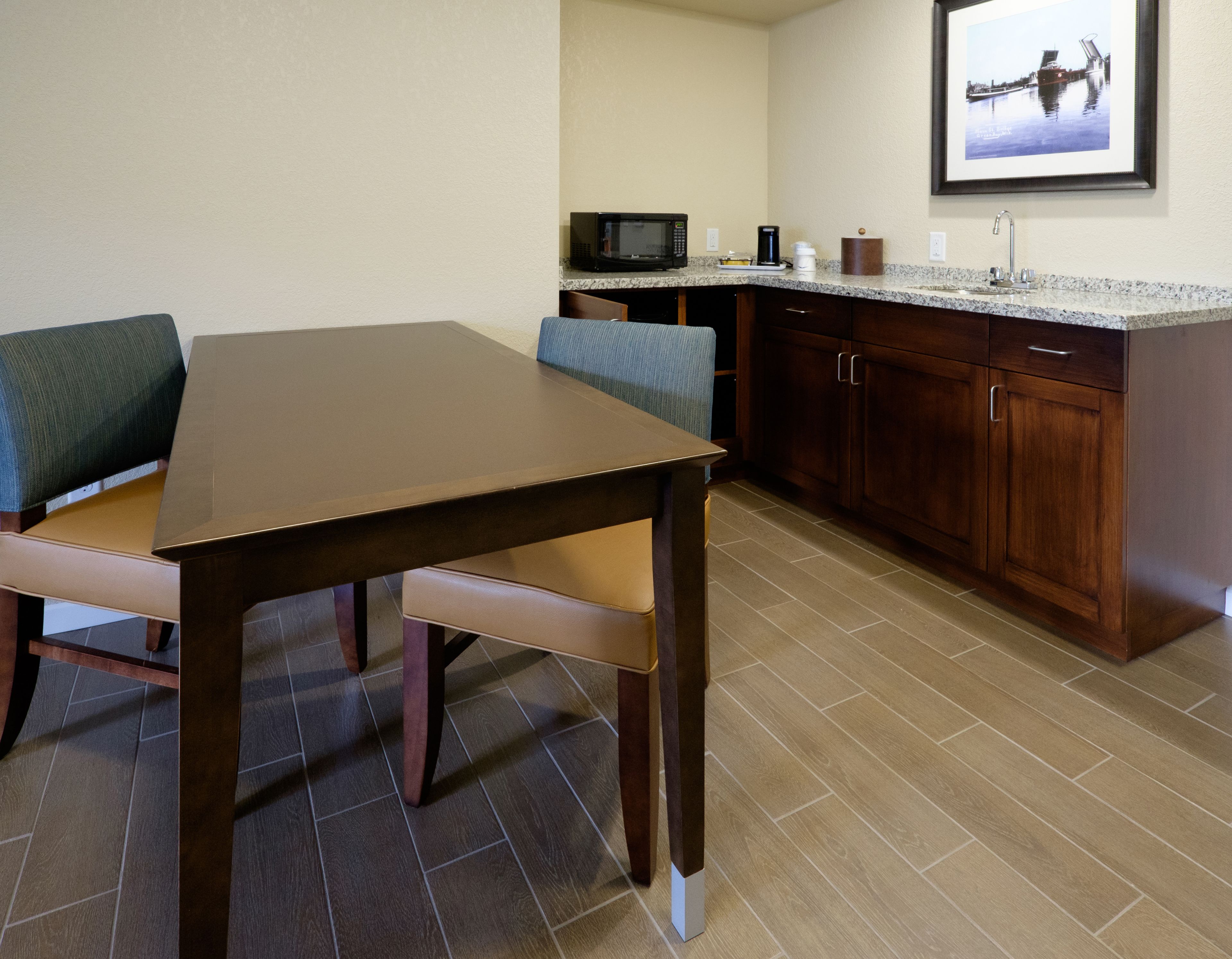 A dining area with a wooden table and chairs, a kitchen with a microwave and cabinets, and a framed picture on the wall.
