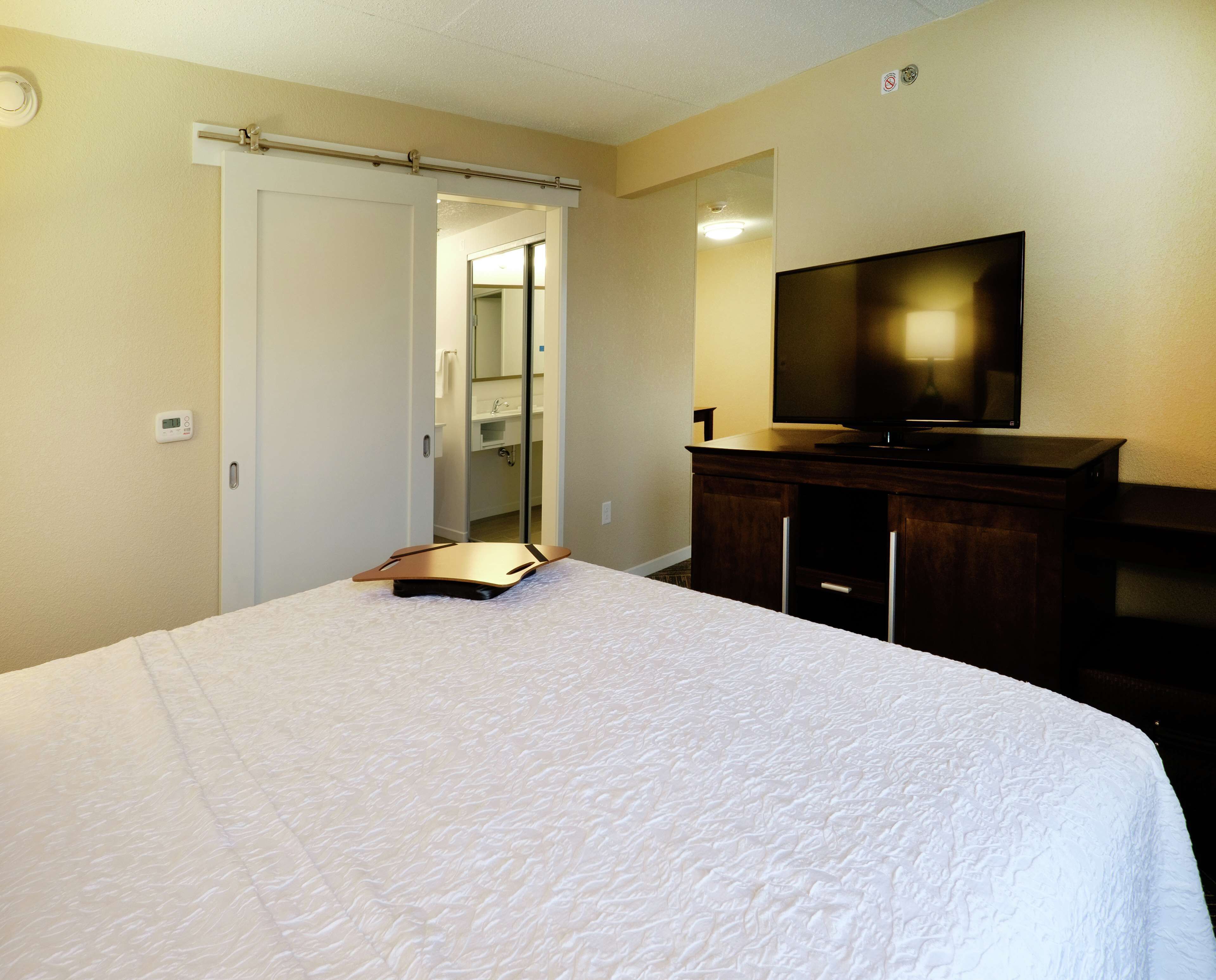Une chambre d’hôtel avec un lit, une télévision, une commode et une salle de bain visible à travers une porte ouverte.