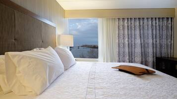 A hotel room with a large bed, a view of a bridge, and a patterned curtain.