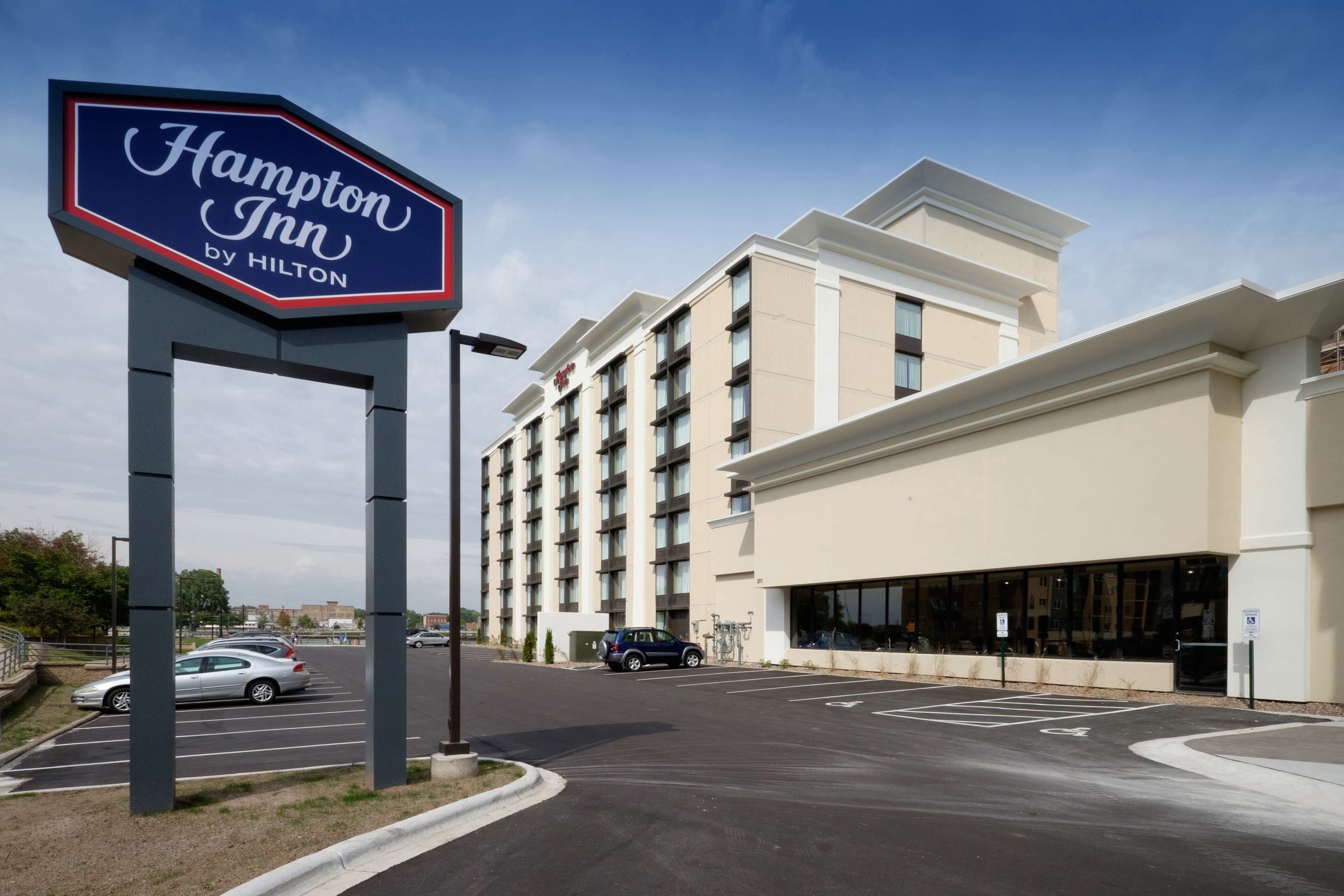 Une enseigne « Hampton Inn by Hilton », un parking et un bâtiment d’hôtel à plusieurs étages doté de grandes fenêtres.
