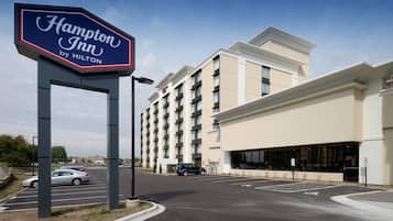Une enseigne « Hampton Inn by Hilton », un parking et un bâtiment d’hôtel à plusieurs étages doté de grandes fenêtres.