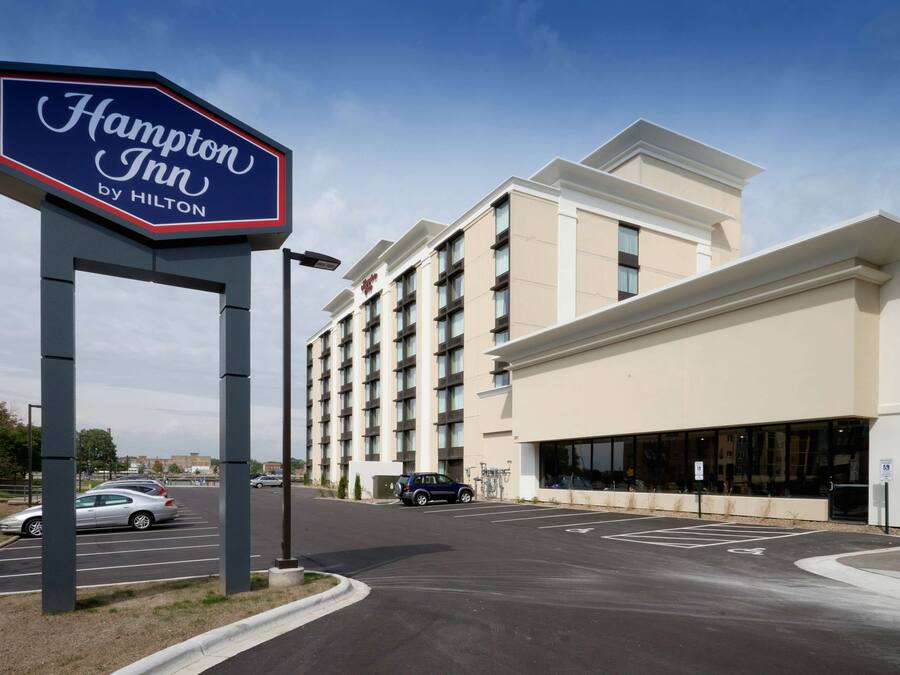 Une enseigne « Hampton Inn by Hilton », un parking et un bâtiment d’hôtel à plusieurs étages doté de grandes fenêtres.
