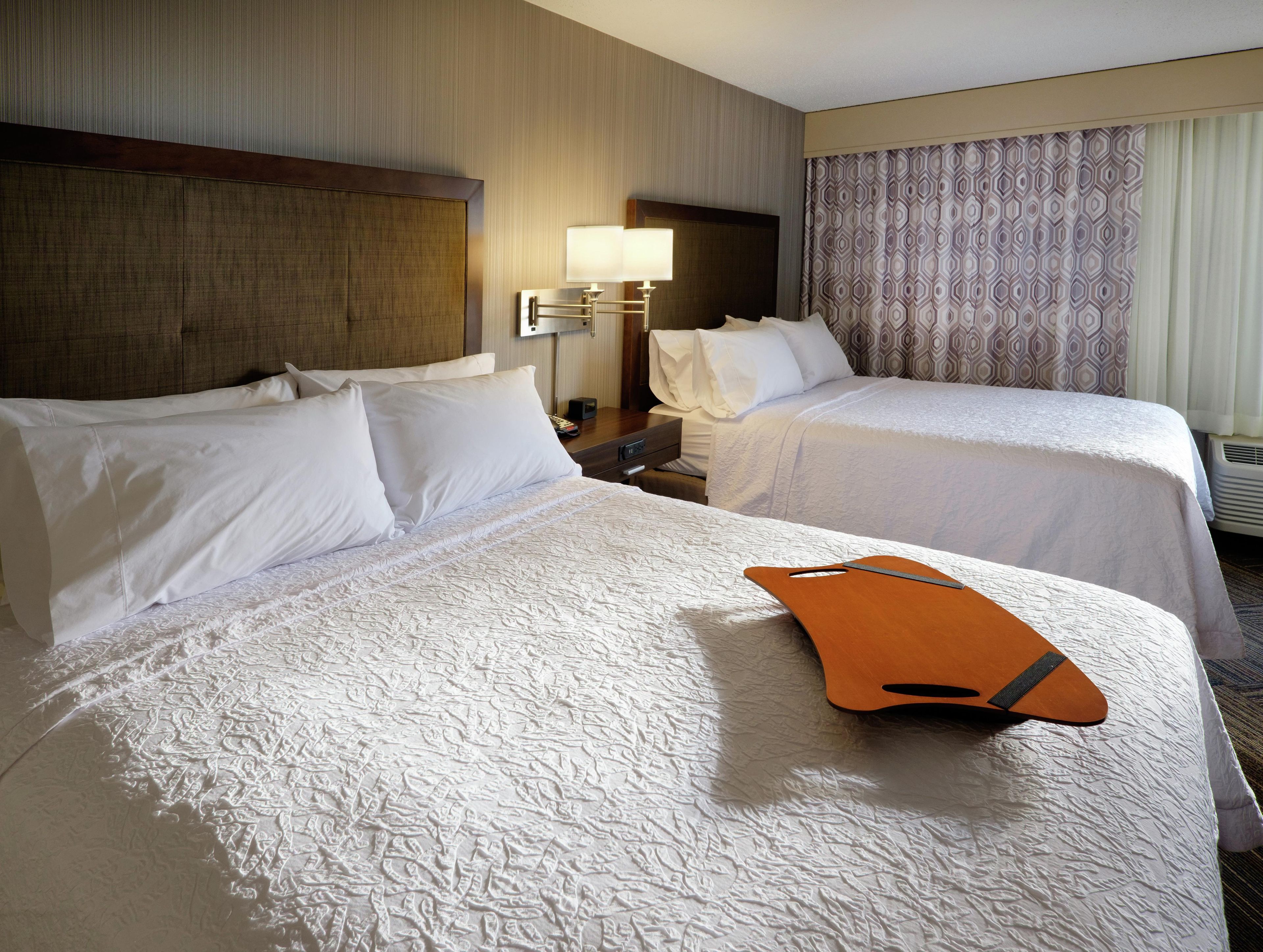Habitación de hotel con dos camas, una mesita de noche, una lámpara y una cortina estampada.