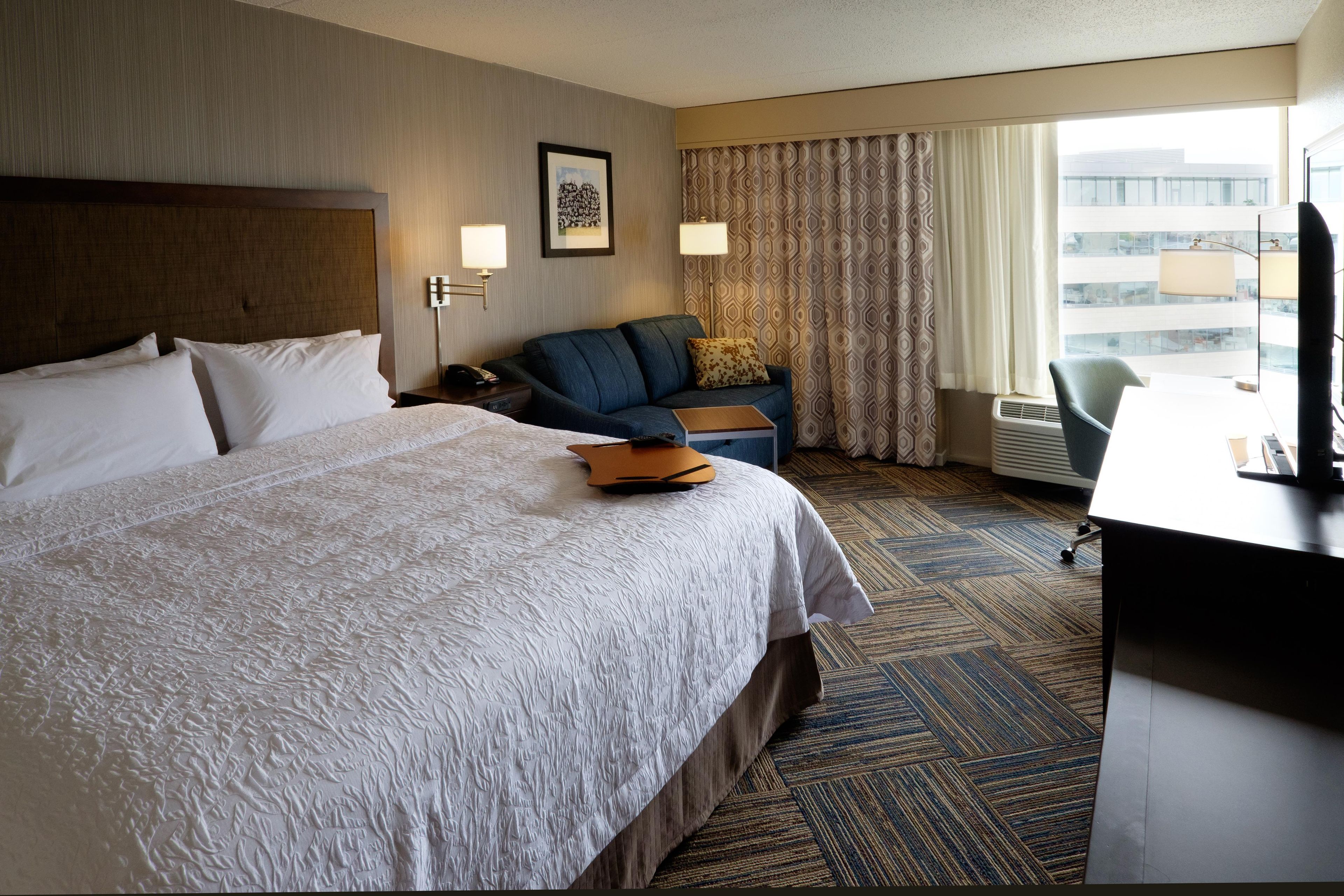 A hotel room with a large bed, a sofa, a desk, and a window with curtains.