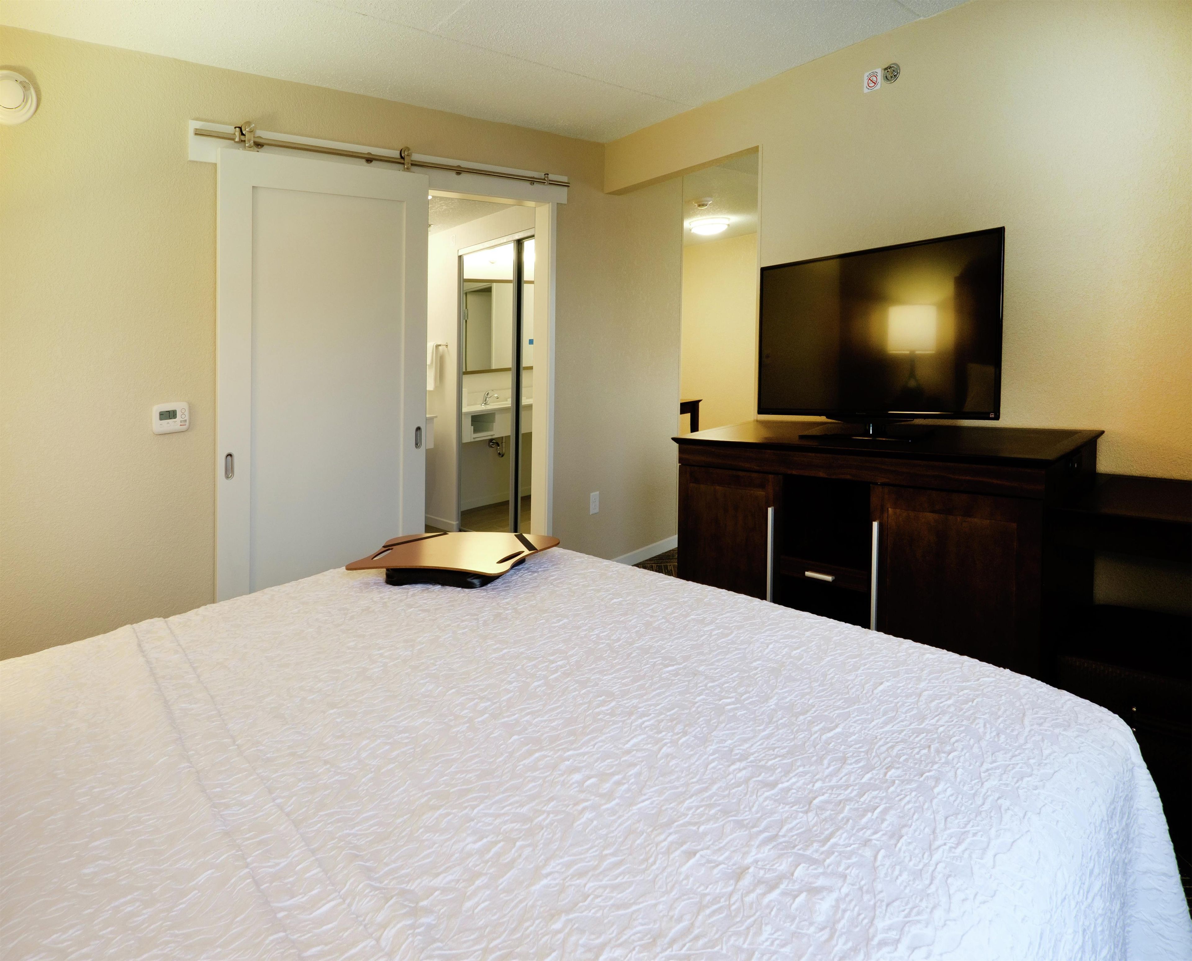Une chambre d’hôtel avec un lit, une télévision, un bureau et une salle de bain, visibles à travers une porte ouverte.