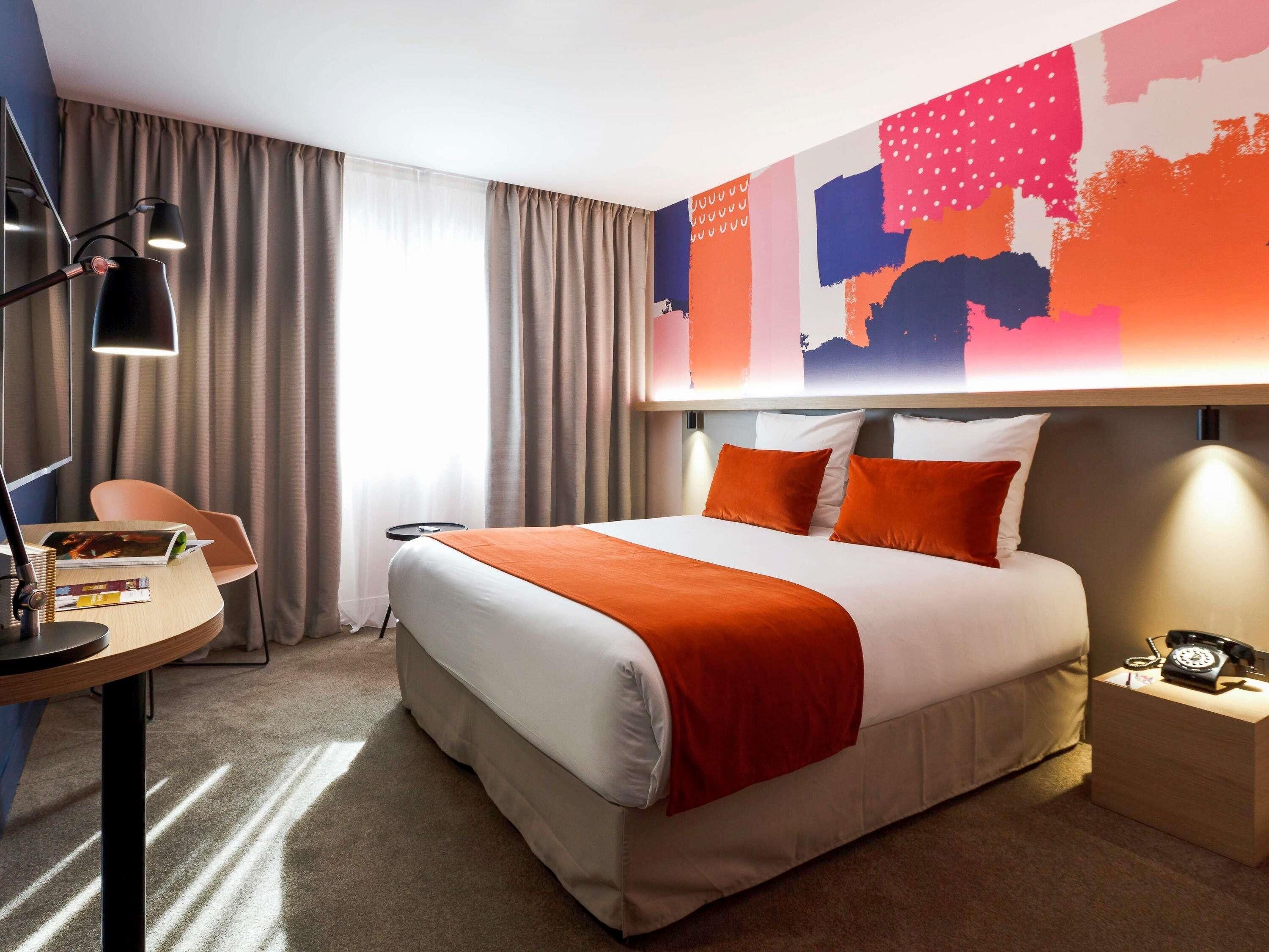 A hotel room with a large bed, a desk with a lamp, a chair, and a map on the wall.