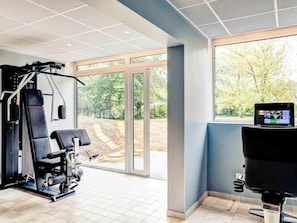 A gym with exercise equipment, large windows, and a view of trees.