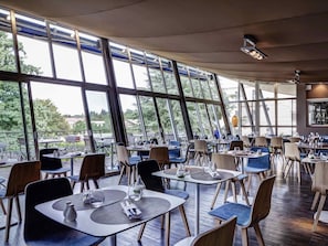 A restaurant with modern interior design, large windows, and a view of the outdoors. - Mercure Lyon Charbonnieres (Charbonnieres-les-Bains)