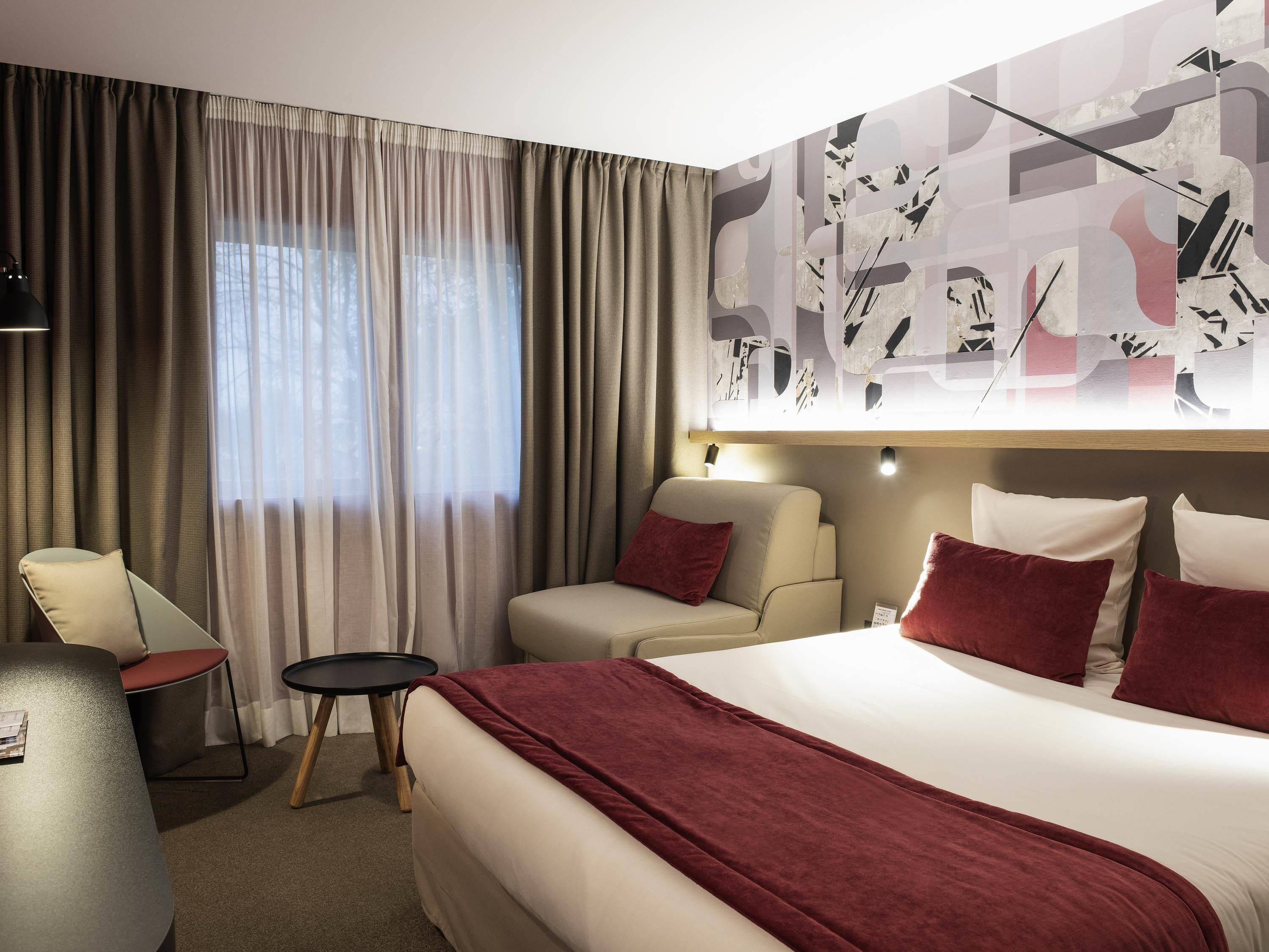A hotel room with a bed, two sofas, a small table, and a large window with curtains.