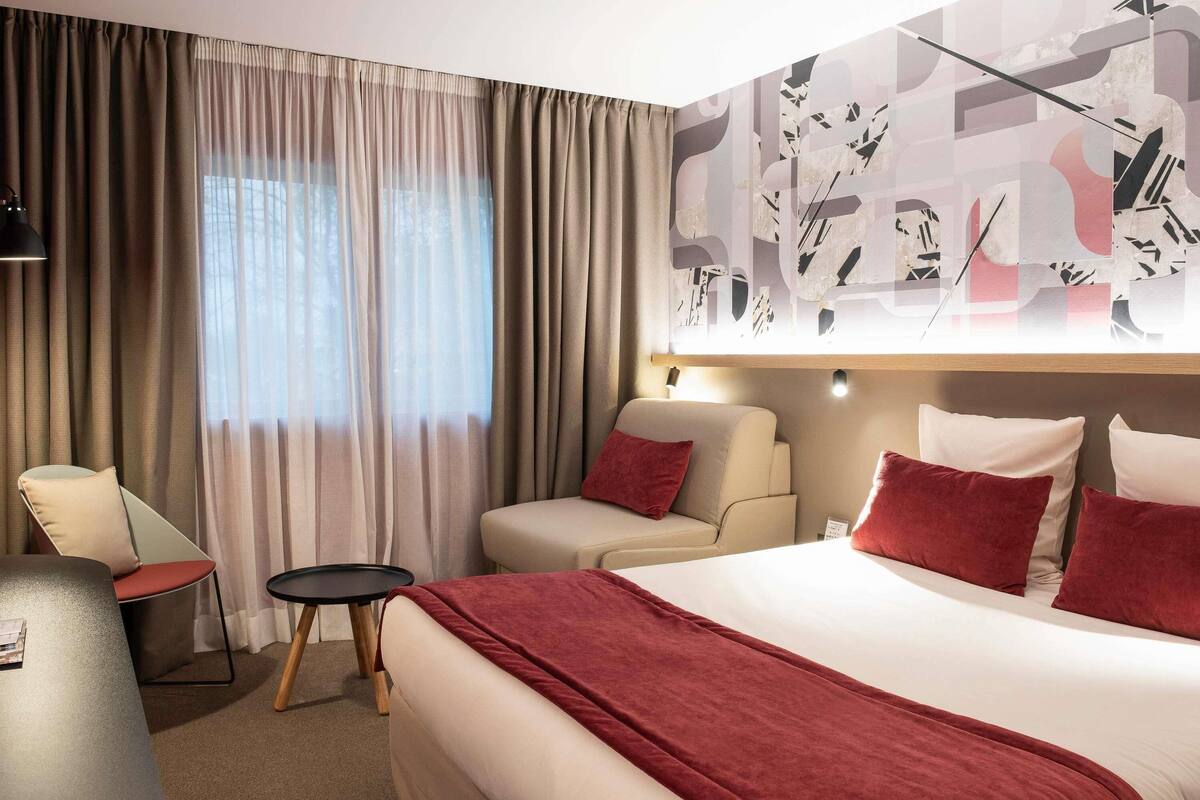 A hotel room with a bed, two sofas, a small table, and a chair.