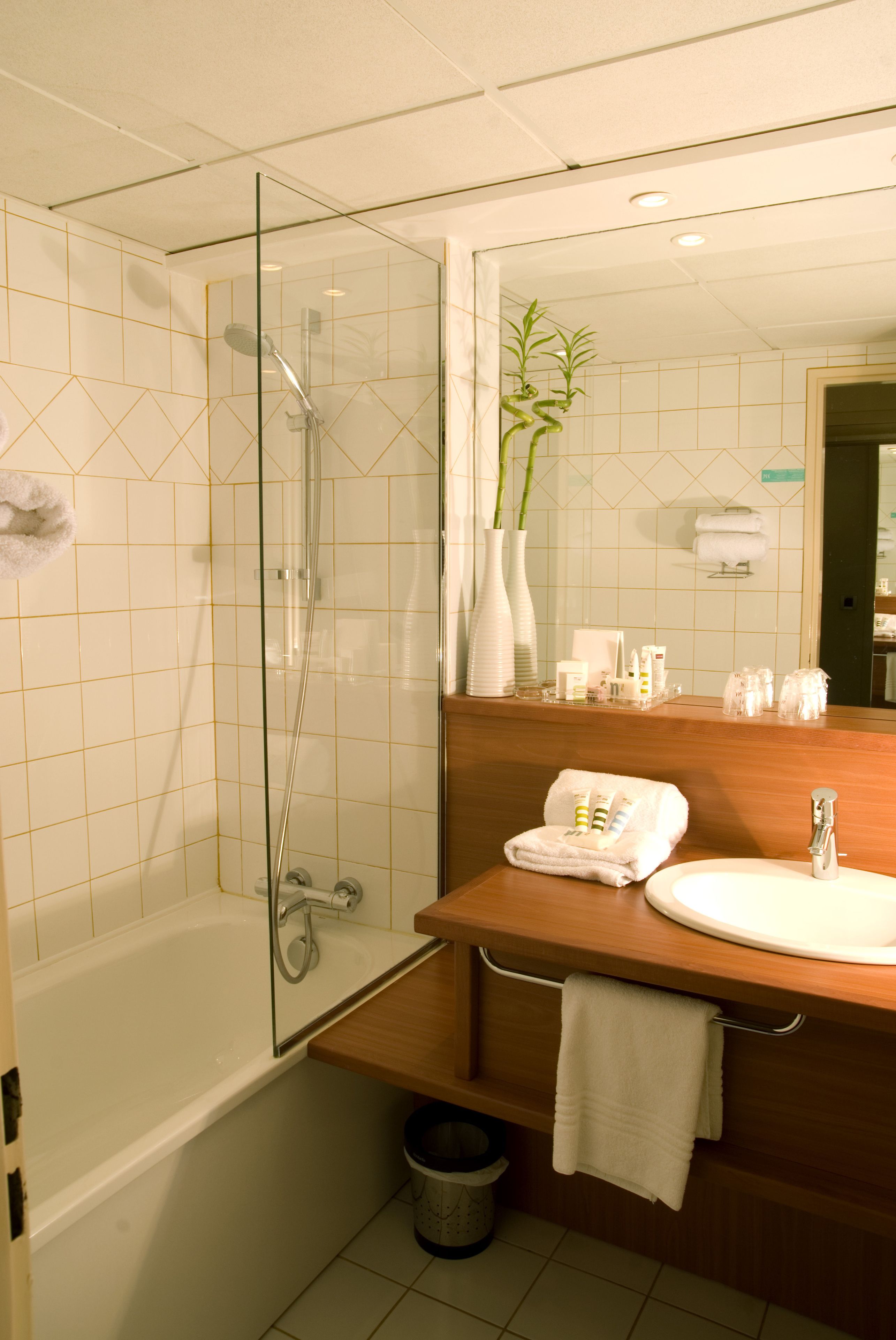 Un baño moderno con ducha de vidrio, tocador de madera con lavamanos y un espejo arriba.