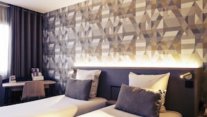 Habitación de hotel con dos camas, un escritorio y una pared con un diseño geométrico.