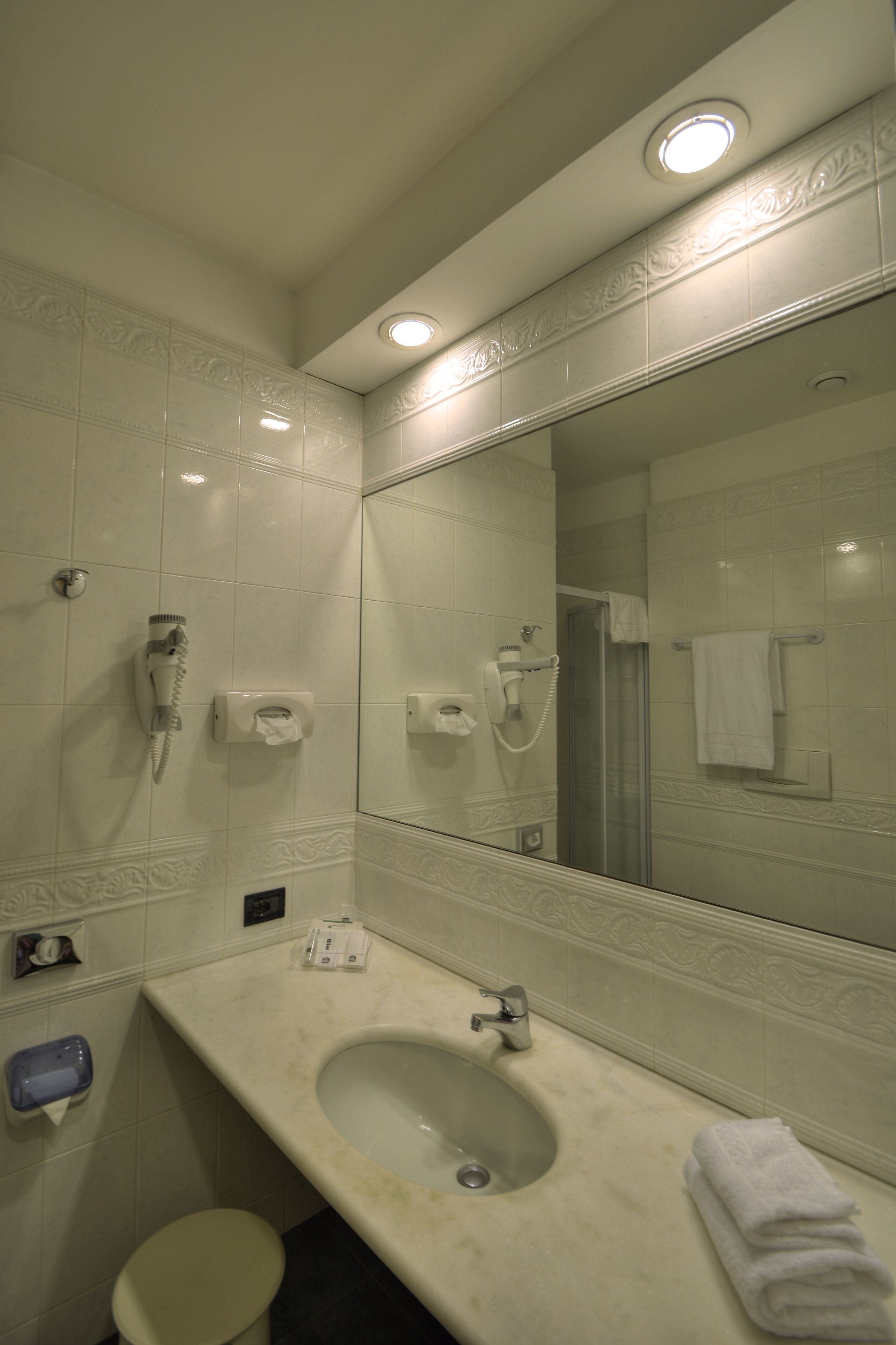 Une salle de bain équipée d’un lavabo, d’un miroir et de deux sèche-cheveux fixés au mur.