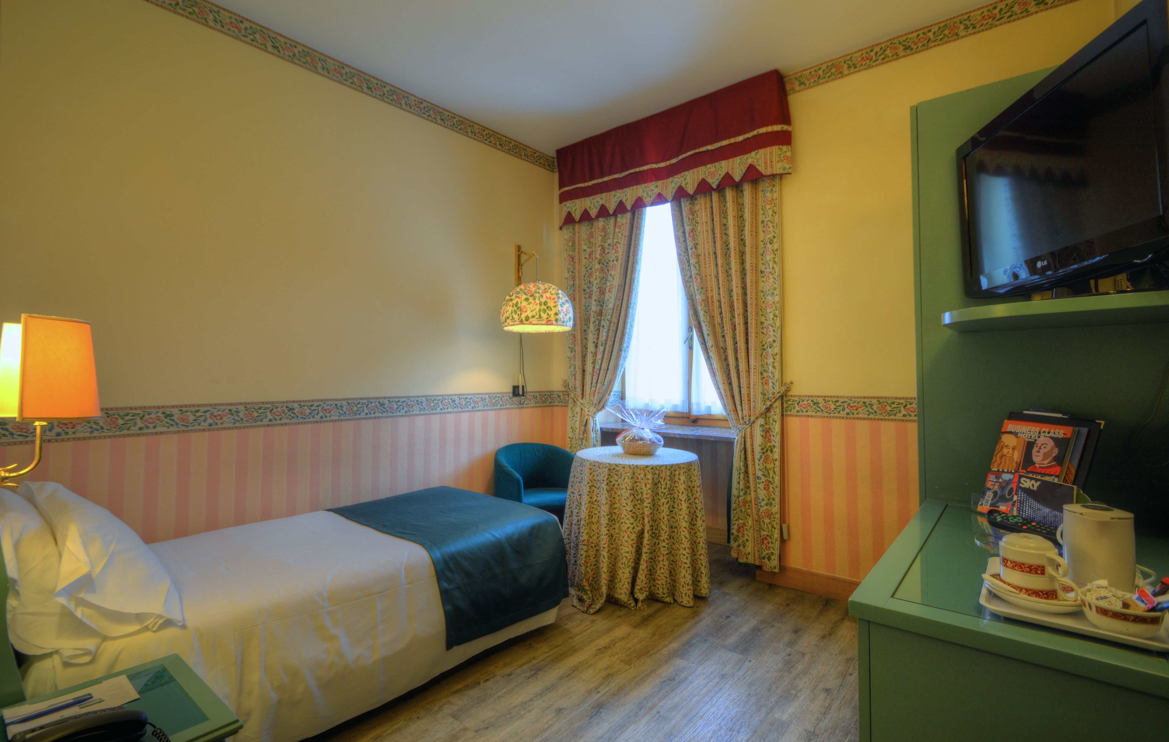 A hotel room with a bed, a small table, a chair, a television, and a window with curtains.