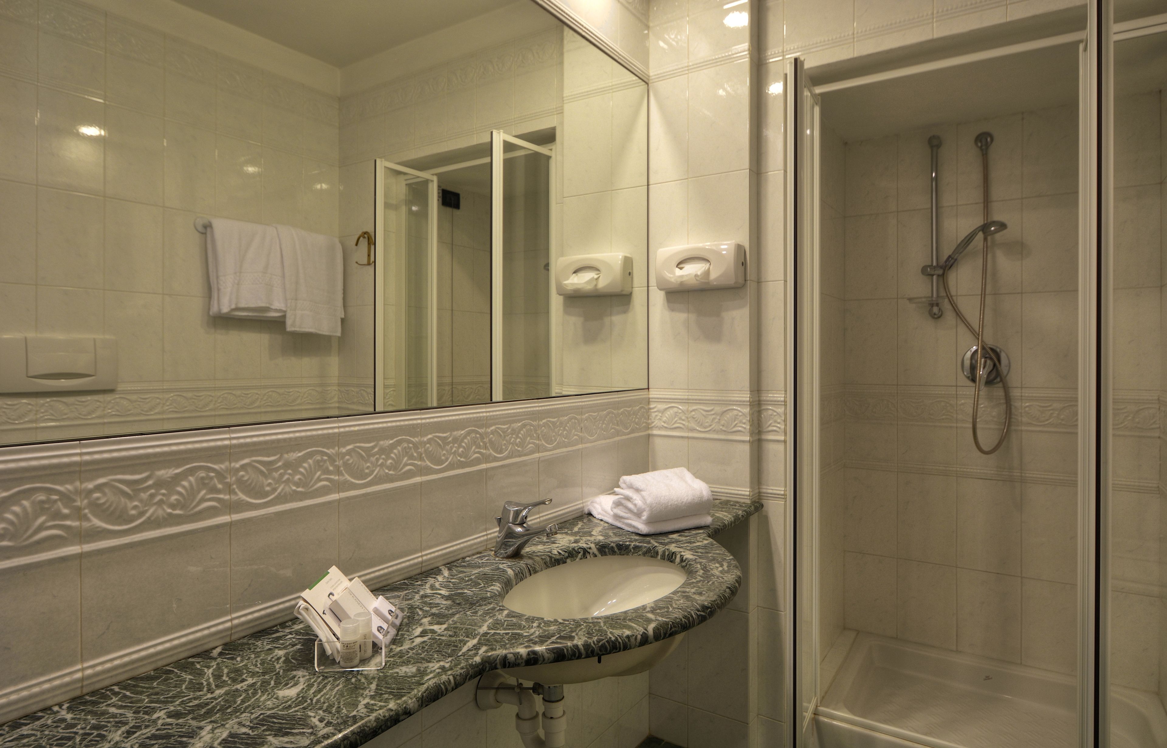 A bathroom with a marble sink, a glass-enclosed shower, and a mirror with a towel hanging on the wall.