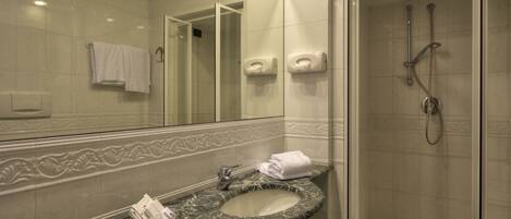 A bathroom with a marble sink, a glass-enclosed shower, and a mirror with a towel hanging on the wall.
