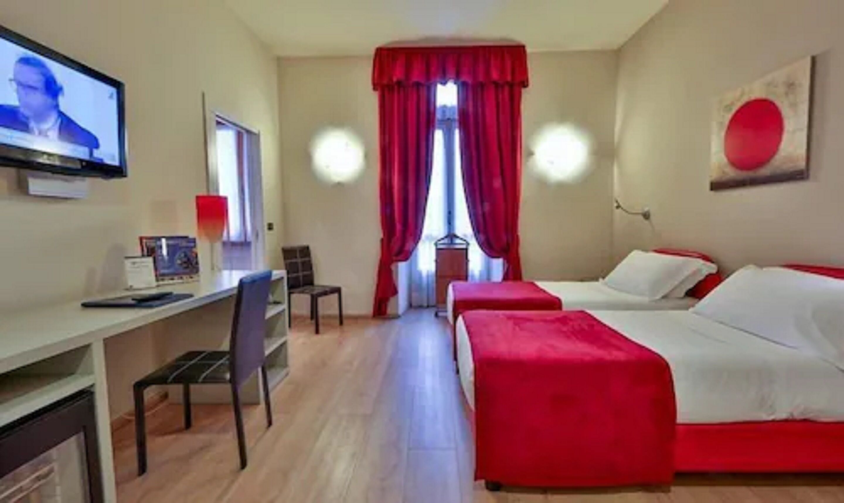 Una camera d'albergo con due letti, una scrivania e una televisione.