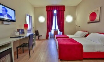 Una camera d'albergo con due letti, una scrivania e una televisione.