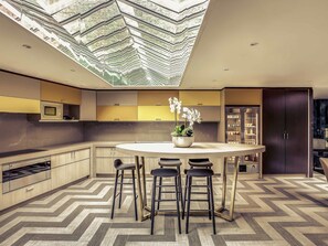 A modern kitchen with a central island, bar stools, and a ceiling skylight. - Mercure Paris Arc de Triomphe Etoile (Paris)