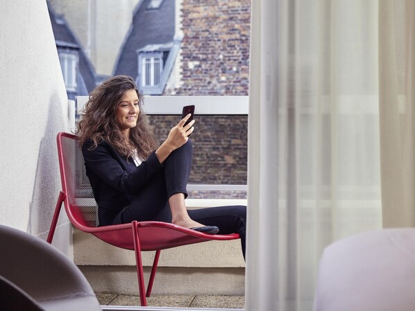 A person sitting on a red chair by a window with a cityscape view.