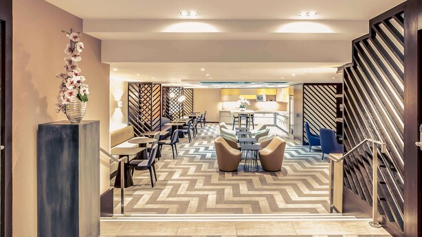 A hotel lobby with a modern design, featuring a central seating area, a staircase, and a decorative wall with a geometric pattern. - Mercure Paris Arc de Triomphe Etoile (Paris)