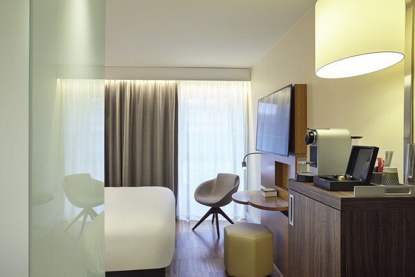 A hotel room with a bed, a desk with a chair, a television, and a minibar. - Mercure Paris Arc de Triomphe Etoile (Paris)