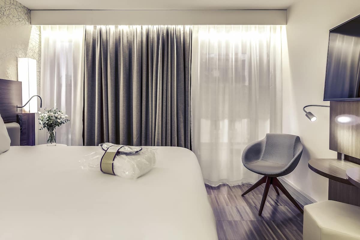 Ein modernes Hotelzimmer mit einem großen Bett, einem Sessel, einem Schreibtisch und einem Fernseher.