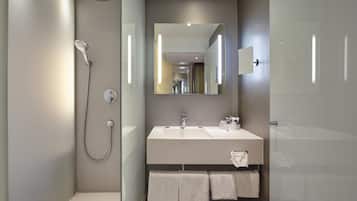 Een moderne badkamer met een glazen douchecabine, een grote spiegel en een wit wastafelmeubel met twee handdoeken.