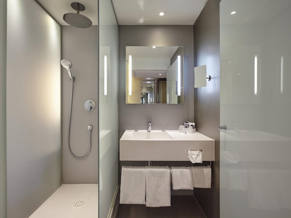 A modern bathroom with a glass shower enclosure, a large mirror, and a white sink with two towels.
