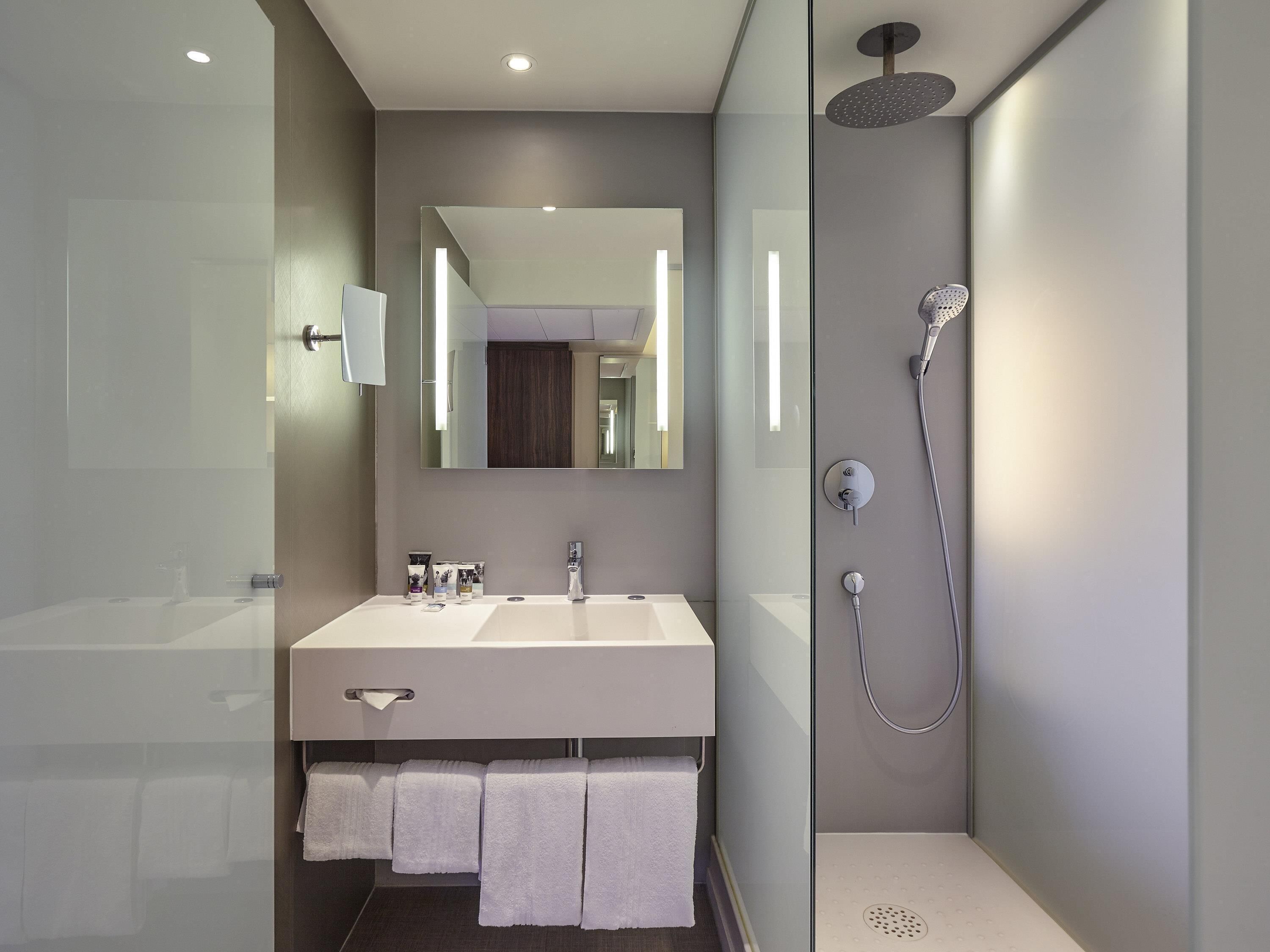 A modern bathroom with a large mirror, a dual sink vanity, and a walk-in shower.