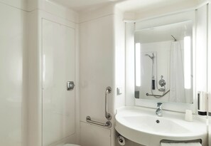 A modern bathroom with a white sink, a mirror, and a shower area.