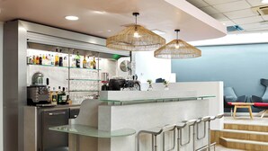 Una zona de bar moderna con una barra de vidrio, electrodomésticos de acero inoxidable y lámparas colgantes de mimbre.