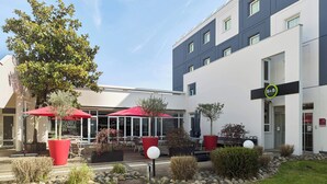 Un hotel moderno con mobiliario exterior, sombrillas rojas y un jardín cuidado.