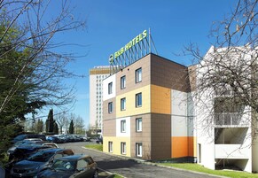 Un hotel tipo casa de huéspedes con diseño moderno, que presenta una estructura de varios pisos y un estacionamiento con varios coches.