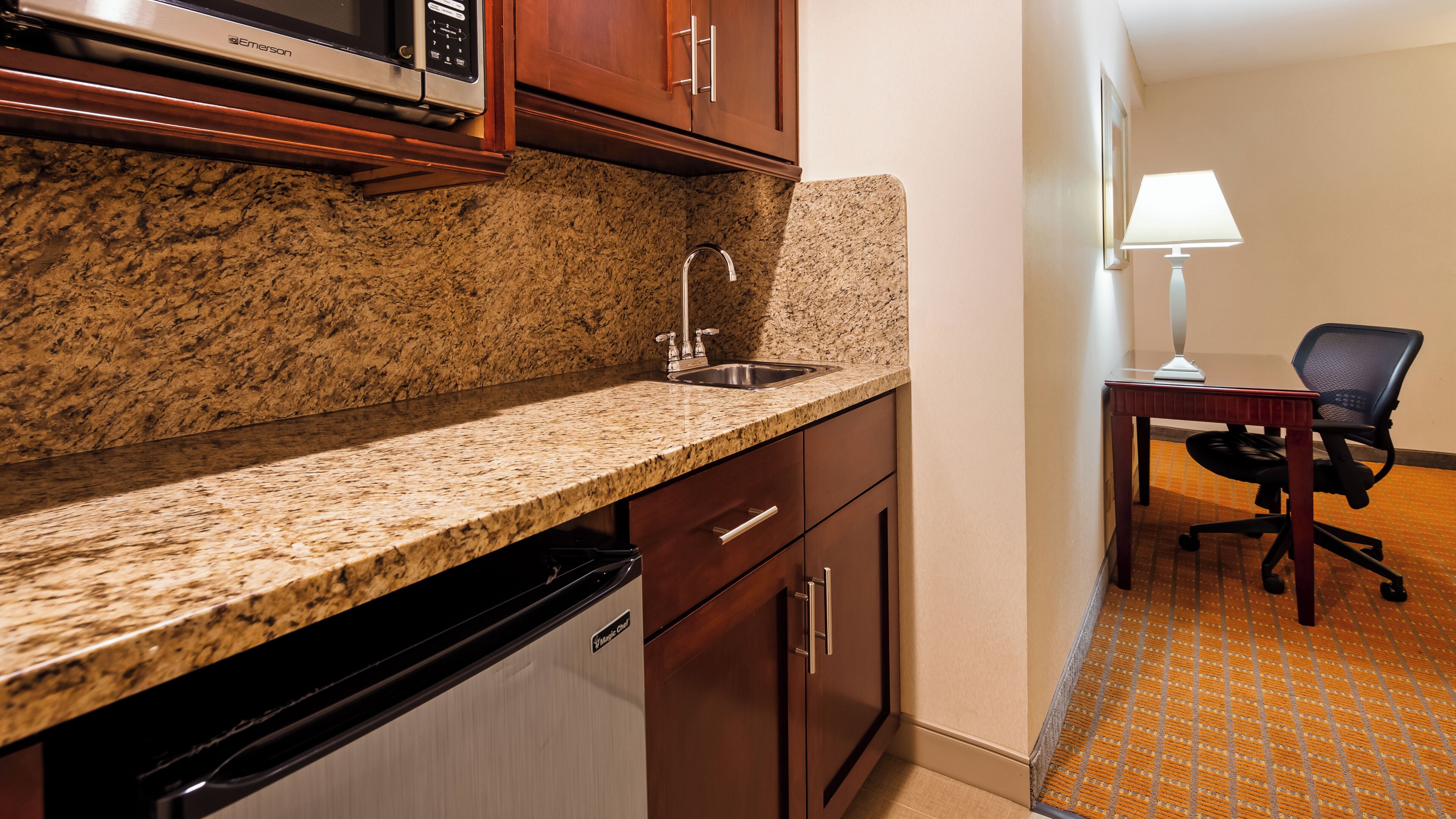 Una cocina con encimeras de granito, pileta de acero inoxidable y muebles de madera.