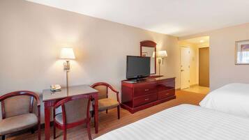 A hotel room with a bed, a desk with a chair, a television, and a dresser.