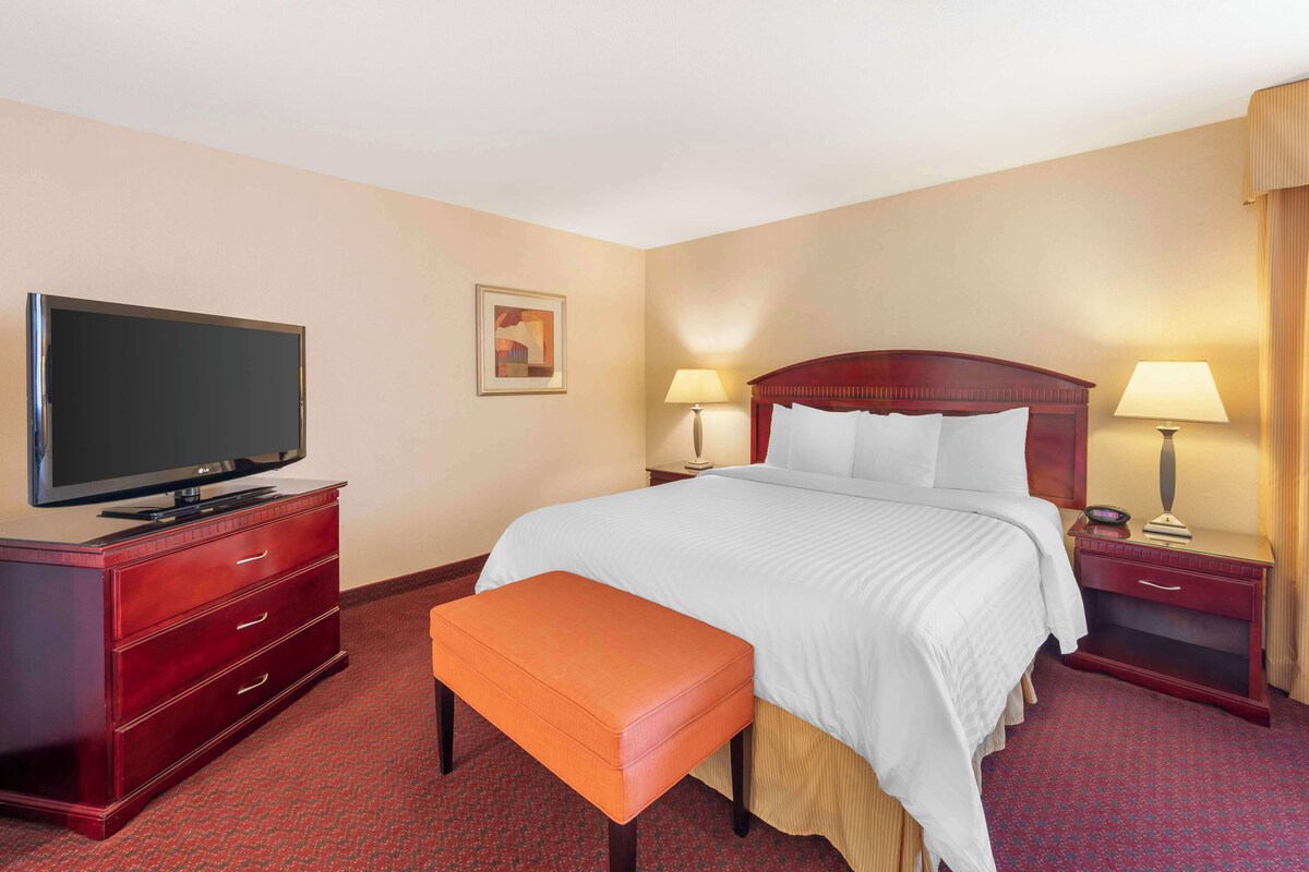 A hotel room with a large bed, a television on a dresser, two bedside lamps, a small table, and a bench.