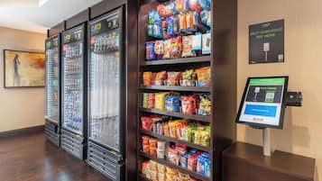 A self-checkout area with a variety of snacks and beverages, a digital payment terminal, and a self-checkout sign.
