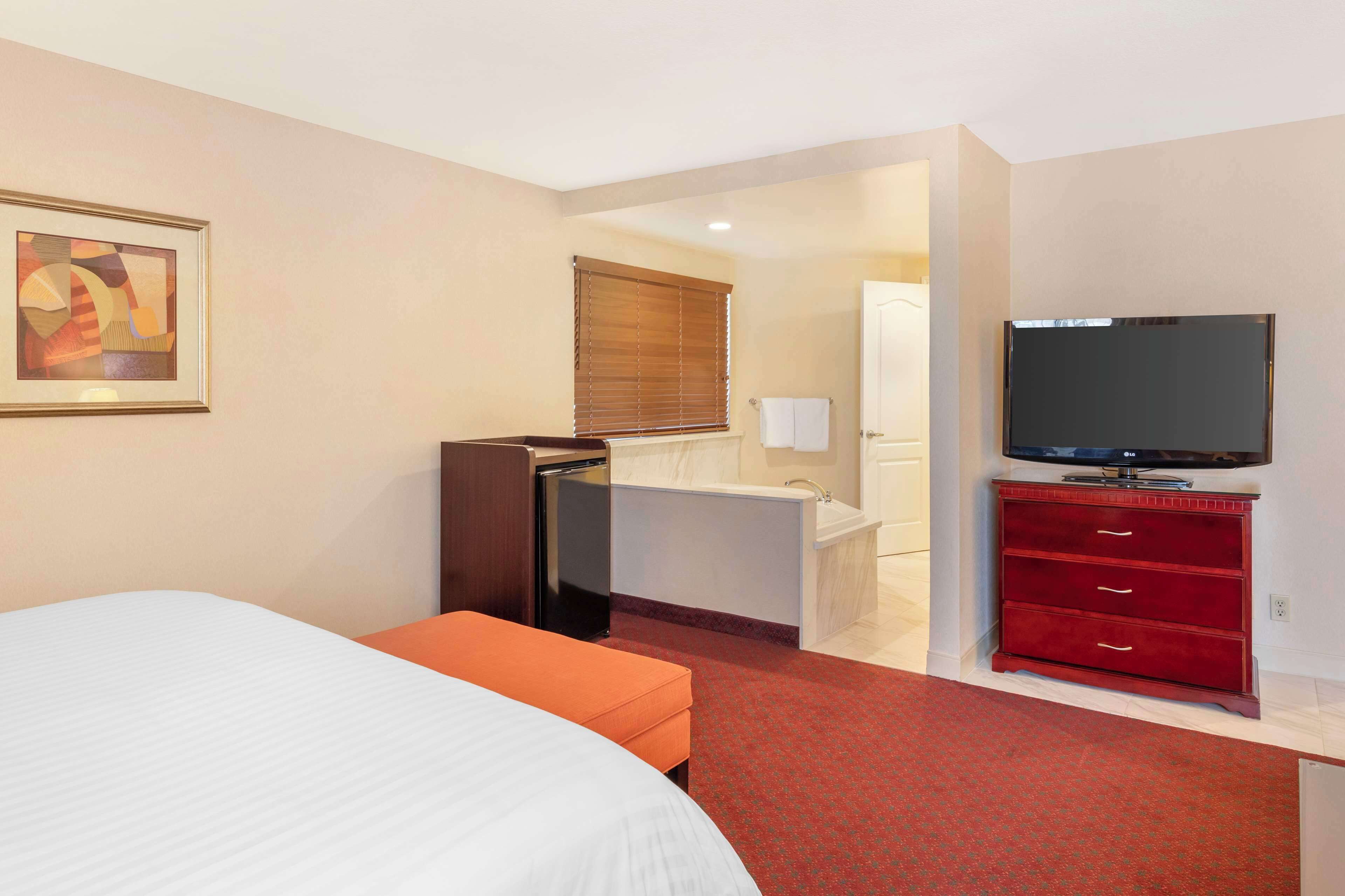 A hotel room with a bed, a desk with a computer, a television, a red dresser, and a bathroom with a bathtub.