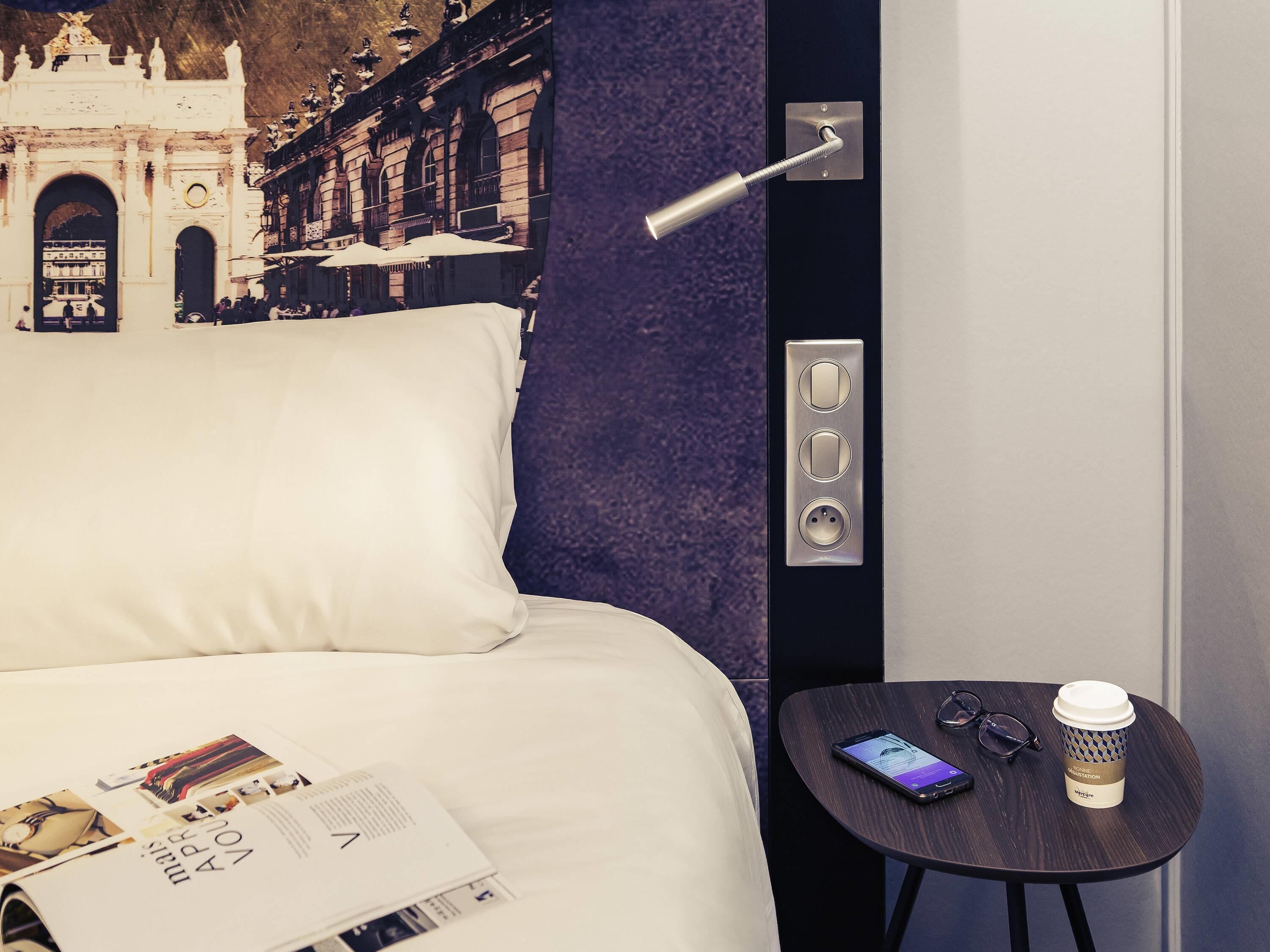Camera d'albergo con un letto, un tavolino con uno smartphone, una tazza di caffè e una rivista.