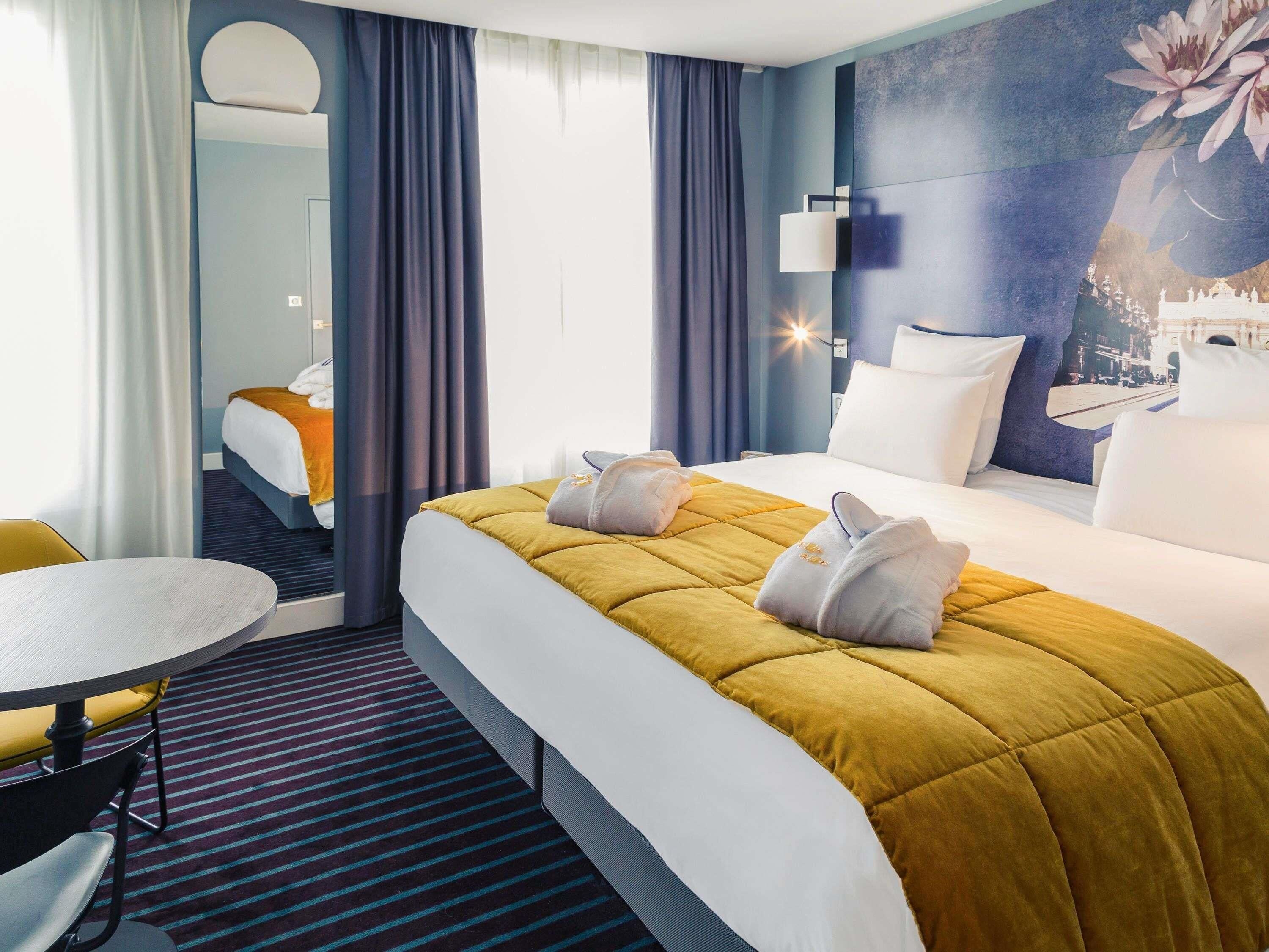 A hotel room with a bed, a table, a chair, and a large window.