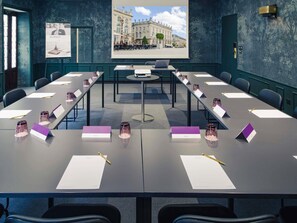 A conference room with a long table, chairs, nameplates, and a projector screen displaying a building image. - Mercure Nancy Centre Place Stanislas Hotel (Nancy)