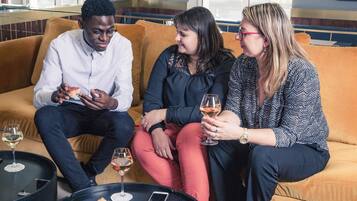 Three people seated on a sofa, a glass of wine, and a plate of food on a table.