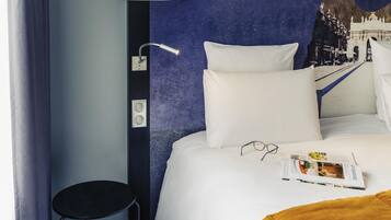 A hotel room with a bed, a black chair, a white pillow, and a magazine on the bed.