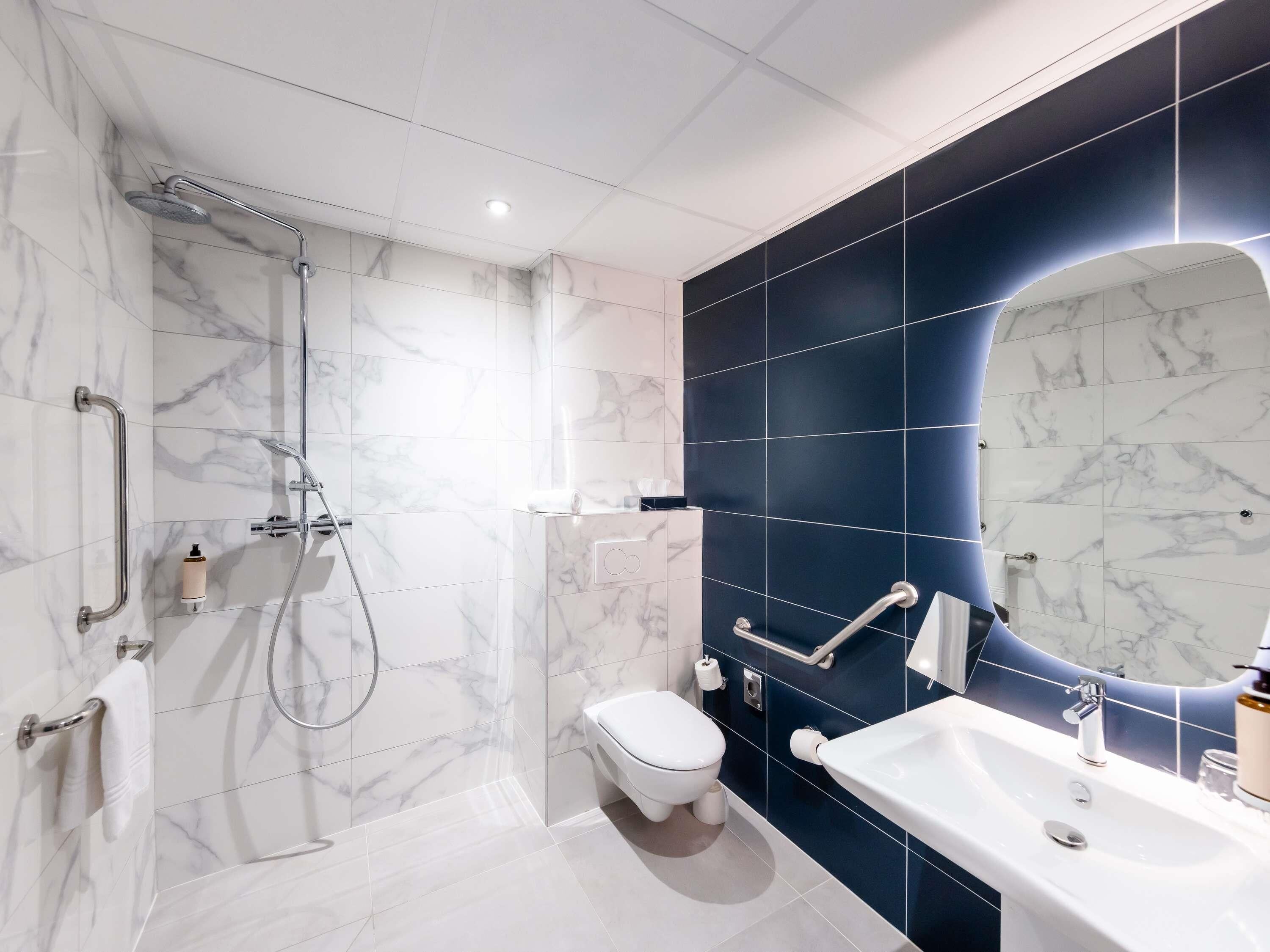 A modern bathroom with a shower, toilet, and sink, featuring marble tiles and a dark accent wall.