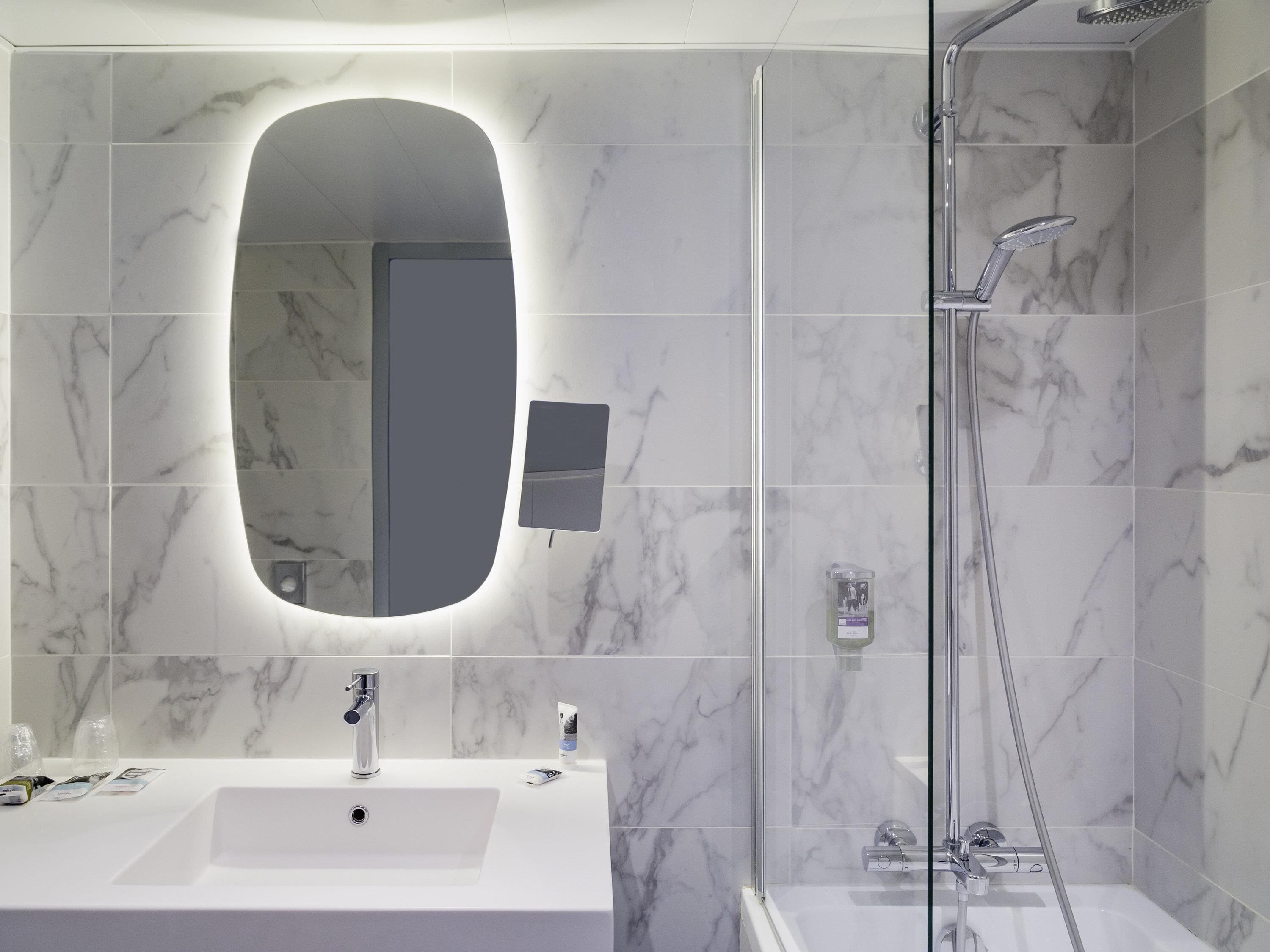 A modern bathroom with a large mirror, a sink, and a shower.
