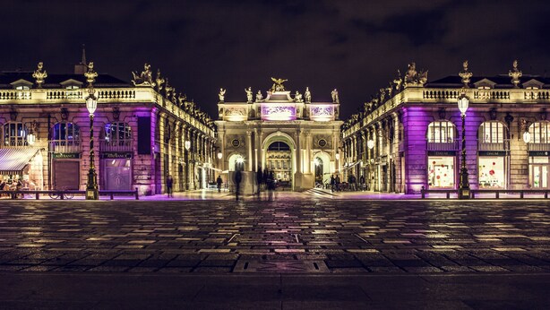 A grand, illuminated building facade with classical architecture, featuring a central archway and statues. - Mercure Nancy Centre Place Stanislas Hotel (Nancy)